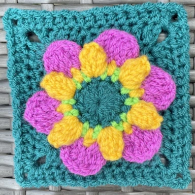The pop flower crochet granny square with a brightly coloured flower in the centre and the border is teal.