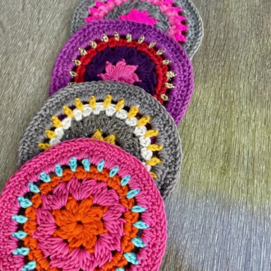four crochet coasters in shades of pink, purple and grey