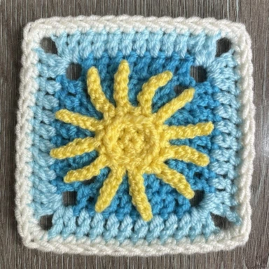 The Sunny Day Crochet Granny Square with a yellow sun in the centre and surrounded by rounds of blue, light blue and white colours.