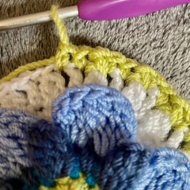 Round 8. Crocheting pale green border around white border. With crochet granny square flower in centre. Close Up