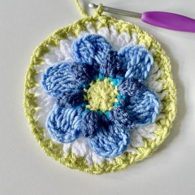 Round 8. Crocheting pale green border around white border. With crochet granny square flower in centre.