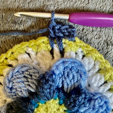 Working blue border around pale green border with blue crochet flower granny square in centre