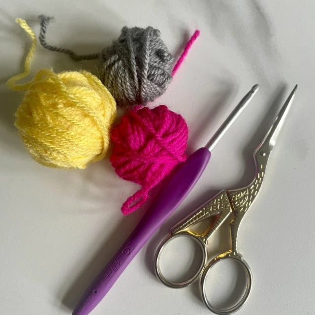 3 little balls of yarn in pink, yellow and grey, a crochet hook and gold scissors